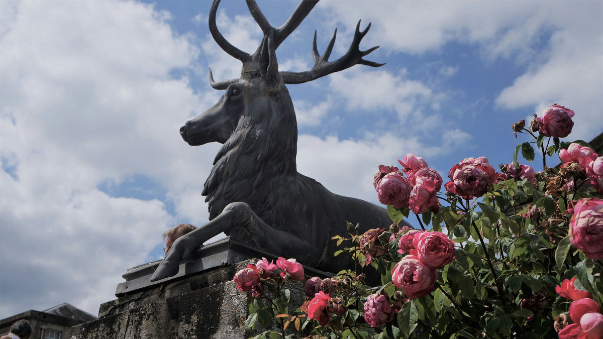 A statue of a deer jumping over a flower bed.