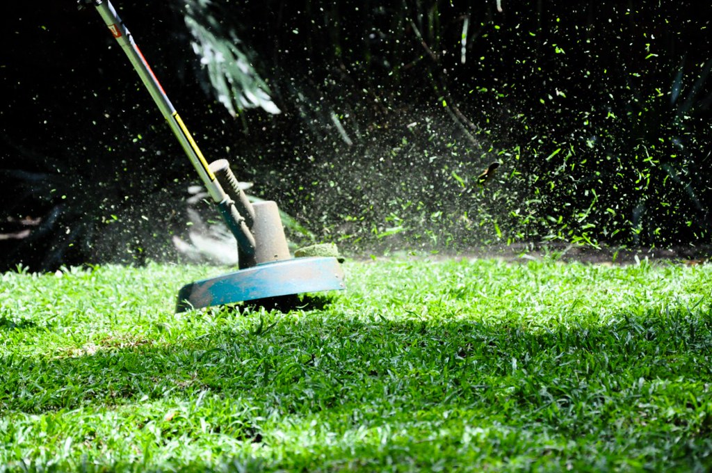 A week wacker is cutting through overgrown edges of a lawn. They're using the weed wacker hack with zip ties to cut the grass more easily.