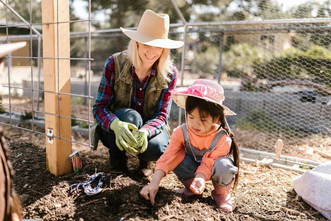 A woman and young child are gardening in mulch on a sunny day. They are learning about weed control in mulch beds.